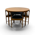 Load image into Gallery viewer, A mid-century modern round dining table with four matching chairs featuring a light wood grain finish and black leather seats, shown on a white studio background.
