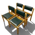 Load image into Gallery viewer, Four wooden dining chairs with dark green padded seats and backrests, arranged together on a light gray studio background.
