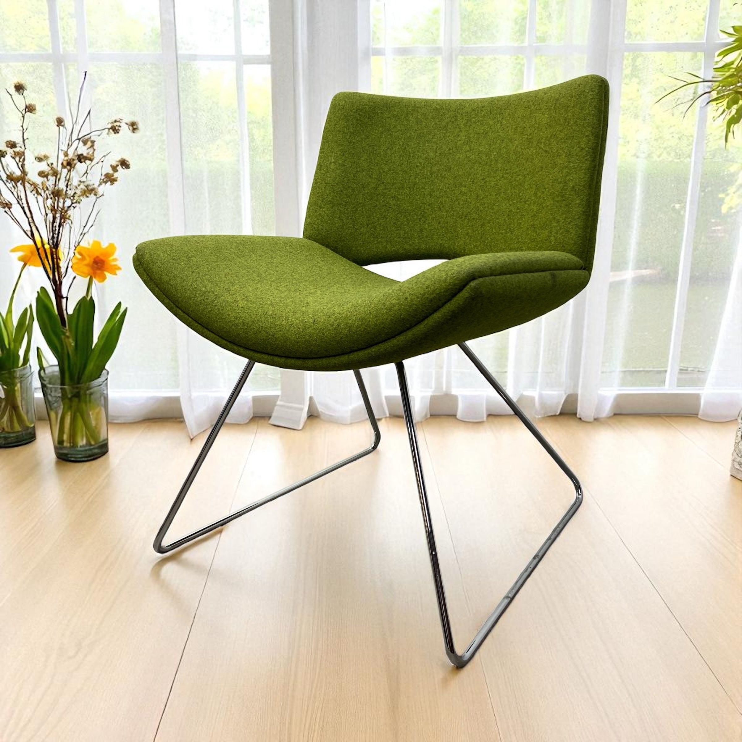 Green chair with metal legs in a room with large windows and plants.