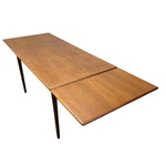 Load image into Gallery viewer, A mid-century modern wooden dining table with a warm brown wood grain finish and slim dark legs, shown on a plain white background.
