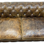 Load image into Gallery viewer, Close-up of a distressed brown leather Chesterfield sofa with button tufting on the backrest and two seat cushions.
