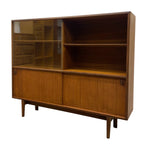 Load image into Gallery viewer, Mid-century modern wooden credenza or hutch with a warm medium-brown wood grain finish, featuring two glass-front cabinet doors on the left, open shelving in the upper right, and two lower cabinet doors with small metal handles, supported by tapered legs.
