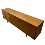 Load image into Gallery viewer, Mid-century modern wooden sideboard with a warm medium-brown finish, featuring five drawers on the left, two cabinet doors in the center, and tapered legs, shown on a plain white background.
