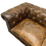 Load image into Gallery viewer, A close-up of a distressed brown leather Chesterfield sofa corner with deep button tufting and a matching cushion, isolated on a white background.

