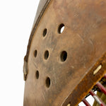 Load image into Gallery viewer, Close-up detail of a rustic brown wooden shield or helmet-like object with circular ventilation holes, showing weathered wood texture and a small portion of red string or cord at the lower right edge against a white background.
