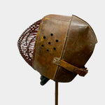 Load image into Gallery viewer, A vintage brown leather and wicker protective helmet displayed on a stand against a light gray background.
