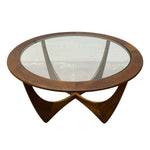 Load image into Gallery viewer, A mid-century modern oval coffee table with a dark walnut wood frame, a clear glass top, and a sculptural interlocking wooden base on a white background.
