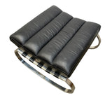 Load image into Gallery viewer, A modern black leather ottoman with a curved polished metal frame and black-and-white checkered leather straps, shown on a plain white background.
