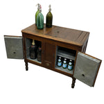 Load image into Gallery viewer, A rustic wooden bar cabinet with two open metal doors, shown on a white background. The cabinet has a dark brown wood body with turned legs and is styled with two green gas bottles on top and several beer bottles inside.
