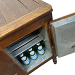 Load image into Gallery viewer, A vintage wooden cabinet with an open metal door revealing three green glass bottles inside, isolated on a white background.
