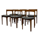 Load image into Gallery viewer, A set of six mid-century modern dining chairs with warm brown wood frames and black upholstered seats, arranged in a group on a white background.

