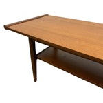 Load image into Gallery viewer, A mid-century modern wooden coffee table with a warm medium-brown wood grain finish, featuring a top shelf and tapered legs, shown against a plain white background.
