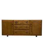 Load image into Gallery viewer, A mid-century modern wooden sideboard or credenza with a warm medium-brown finish, featuring a left cabinet door, a center stack of three drawers with oval pulls, and a right cabinet door, shown on a plain white background.
