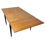 Load image into Gallery viewer, A mid-century modern extendable wooden dining table with a warm medium-brown teak wood grain finish and dark tapered legs, shown on a plain white background.
