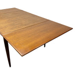 Load image into Gallery viewer, A mid-century modern wooden extendable table with a warm medium-brown wood grain finish and dark tapered legs, shown on a plain white background.
