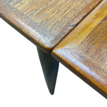 Load image into Gallery viewer, Close-up detail of a mid-century modern wooden table corner, showing the polished wood grain top and a dark tapered metal leg against a white background.

