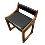 Load image into Gallery viewer, A mid-century modern wooden dining chair with a warm brown wood frame and black leather seat and backrest cushions, shown on a plain white background.

