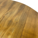 Load image into Gallery viewer, Close-up of a round wooden table showing the warm golden-brown wood grain and a visible center seam between two planks, with a white background in the upper right corner.
