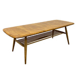 Load image into Gallery viewer, A mid-century modern wooden coffee table with a warm brown finish, featuring a rounded rectangular top, angled legs, and a slatted lower shelf, shown on a plain white background.
