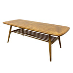 Load image into Gallery viewer, A mid-century modern wooden coffee table with a natural oak finish, featuring a rounded rectangular top, angled legs, and a slatted lower shelf, shown on a plain white background.
