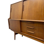 Load image into Gallery viewer, Mid-century modern wooden sideboard cabinet with a warm medium-brown finish, featuring two upper doors with vertical handles, one lower door, three drawers with horizontal handles, and a tapered leg.
