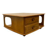 Load image into Gallery viewer, A mid-century modern wooden coffee table with two drawers, open side shelves, and small black caster wheels, shown on a plain white background.
