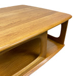 Load image into Gallery viewer, A close-up of a mid-century modern wooden coffee table with a warm honey finish, showcasing the wood grain, curved edges, and open shelf design against a solid white background.
