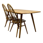 Load image into Gallery viewer, A mid-century modern wooden dining table with two matching spindle-back chairs, shown on a plain white background.
