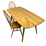 Load image into Gallery viewer, A mid-century modern wooden dining table with rounded corners and four tapered legs, accompanied by two matching wooden spindle-back chairs, shown on a plain white background.
