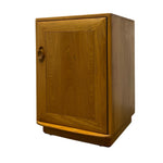Load image into Gallery viewer, A mid-century modern wooden cabinet with a warm honey-toned finish, featuring a circular pull handle and a small footrest, shown on a plain white background.
