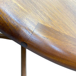 Load image into Gallery viewer, Close-up detail of a polished medium-brown wooden table showing the wood grain, a circular mounting hole, and a seam on the tabletop, with a light-colored metal support leg visible against a white background.
