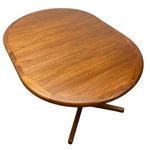 Load image into Gallery viewer, An oval wooden dining table with a warm medium-brown teak wood finish and a distinctive four-star metal pedestal base, shown on a solid white background.
