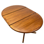 Load image into Gallery viewer, A mid-century modern oval wooden table with three drop-leaf panels, featuring a warm medium-brown wood grain finish and a folding tripod base, shown on a solid white background.

