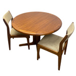 Load image into Gallery viewer, A mid-century modern dining set featuring a round wooden table and two matching chairs with beige upholstered seats and backs, shown on a plain white background.
