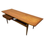 Load image into Gallery viewer, Mid-century modern wooden writing desk with a warm walnut finish, featuring a single drawer on the left with a dark wood drawer front and a lower open shelf, shown on a plain white background.
