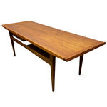Load image into Gallery viewer, A mid-century modern wooden coffee table with a warm medium-brown wood grain finish, tapered legs, and a lower shelf, shown on a plain white background.
