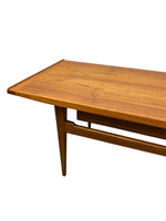 Load image into Gallery viewer, A close-up of a mid-century modern wooden table with a warm honey-brown finish, showcasing the wood grain and a tapered leg against a plain white background.
