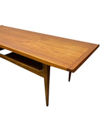 Load image into Gallery viewer, A mid-century modern wooden coffee table with a warm medium-brown walnut finish, featuring tapered legs and a lower shelf, shown against a plain white background.
