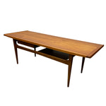 Load image into Gallery viewer, A mid-century modern wooden writing desk with a warm medium-brown walnut finish, featuring a top drawer, open shelf, and tapered legs, shown on a plain white background.
