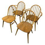 Load image into Gallery viewer, Four wooden dining chairs with spindle backs and curved armrests, shown on a plain white background.
