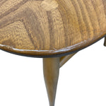 Load image into Gallery viewer, Close-up detail of a round wooden table top with a visible circular knot and a glossy finish, showing part of the curved edge and a tapered wooden leg against a white background.
