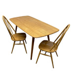 Load image into Gallery viewer, A mid-century modern dining set featuring a rectangular wood table with rounded corners and two matching spindle-back chairs, shown on a plain white background.
