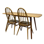 Load image into Gallery viewer, A mid-century modern wooden dining table with two matching spindle-back chairs, shown against a plain white background.
