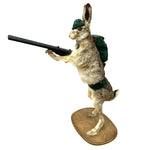 Load image into Gallery viewer, A taxidermy-style rabbit figurine standing on a wooden base, wearing a green hat and backpack and holding a black rifle, isolated on a white background.
