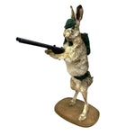 Load image into Gallery viewer, A taxidermy-style rabbit figurine standing on its hind legs and holding a black rifle, dressed in a green beret and green backpack, mounted on an oval wooden base against a plain white background.
