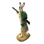 Load image into Gallery viewer, A taxidermy rabbit figurine standing on a wooden base, wearing a green backpack and holding a rifle, isolated on a white background.
