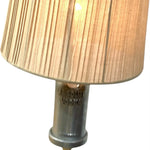 Load image into Gallery viewer, A close-up of a table lamp featuring a pleated beige fabric shade and a brushed silver metal base with 'ABSOLUT VODKA' embossed on the neck, set against a plain white background.
