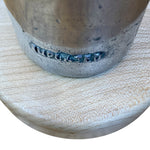 Load image into Gallery viewer, Close-up of a rustic metal and concrete planter pot with the word 'IMPORTED' carved into the side, resting on a light-colored wooden surface against a white background.
