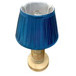 Load image into Gallery viewer, A table lamp with a pleated blue fabric shade, a clear glass bottle base printed with 'Absolut Vodka', and a round light wood foot.
