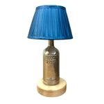 Load image into Gallery viewer, A table lamp featuring a blue pleated fabric shade on a metallic Absolut Vodka bottle base, set on a round light wood pedestal against a white background.

